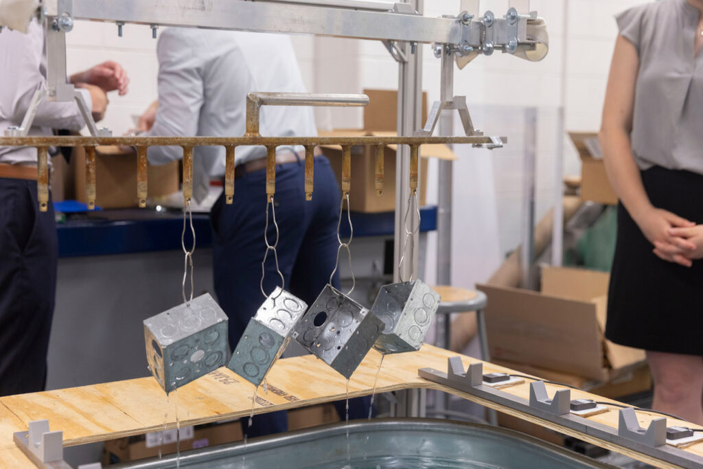 Photo of metal parts being lifted from a tub of liquid in a demonstration of a machine developed by UW-Stout students in their engineering capstone course.