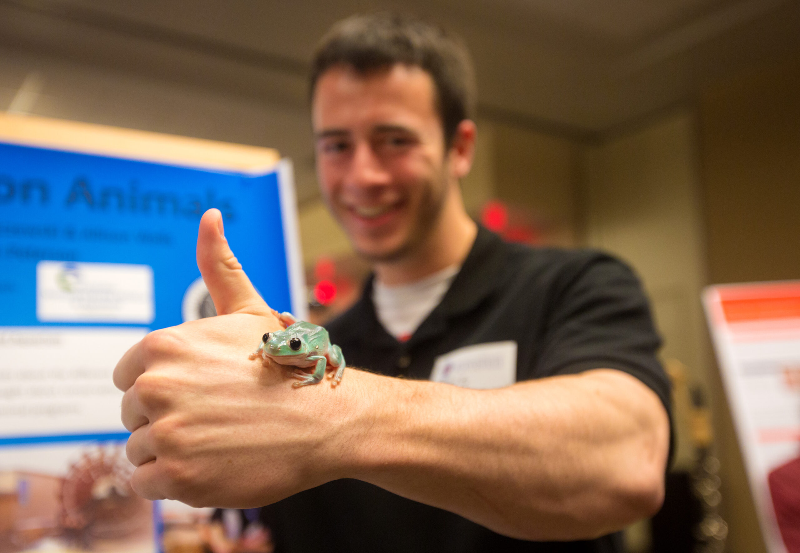 A student standing in front of a poster with frog on hand.